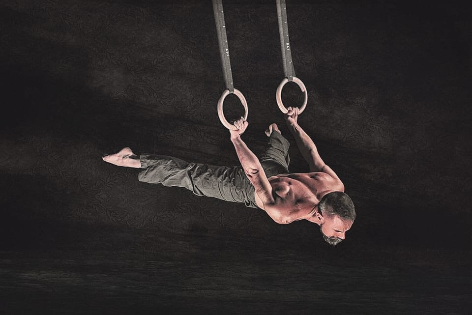 Mat Harvey holding a horizontal position below gymnastic rings in a black studio